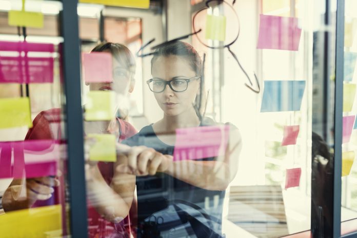 Two business women working together on wall glass