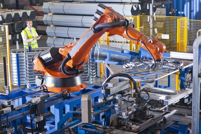 Worker controlling robotic machinery lifting steel fencing on production line in manufacturing plant