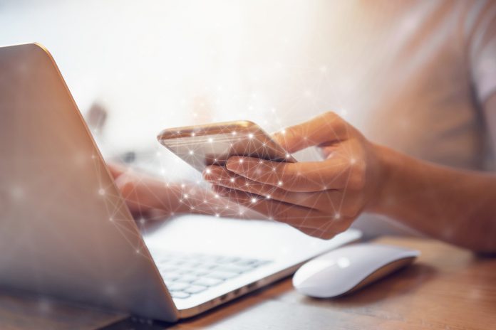 Woman hand holding mobile phone and laptop data synchronization