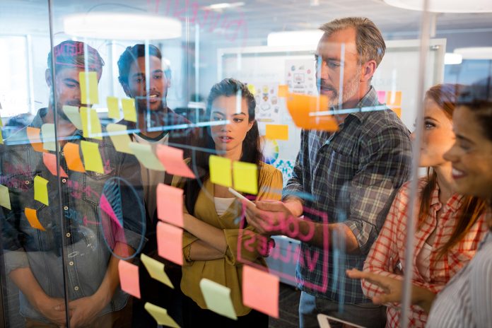 Creative business team looking at sticky notes on glass window