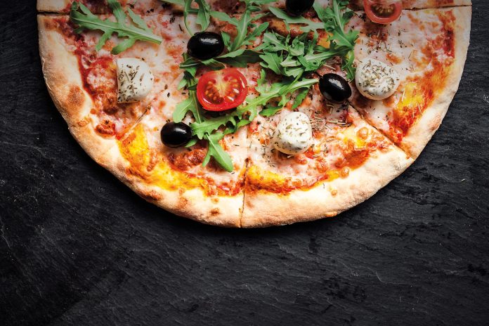 Pizza with tomatoes, mozzarella cheese and arugula. Pizza menu.Top view with copy space on dark stone table